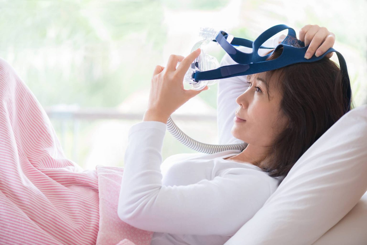 A woman in bed taking off her CPAP machine for sleep apnea.