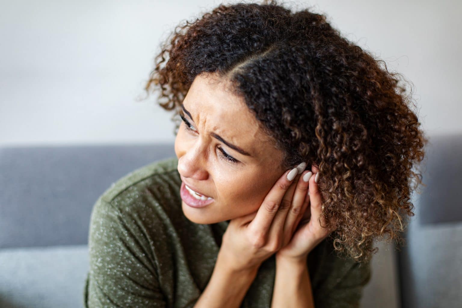 Woman experiencing ear pain, holding hands up to her ears.