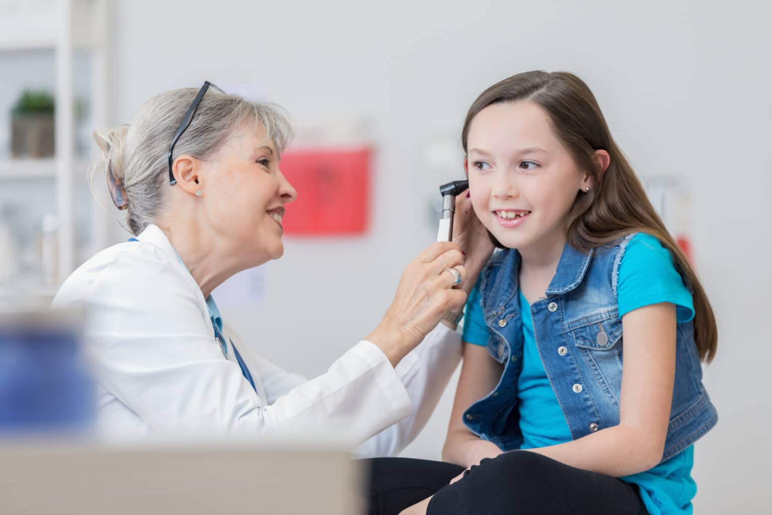 Cheerful senior pediatrician uses an otoscope to check patient's ear during medical examination.