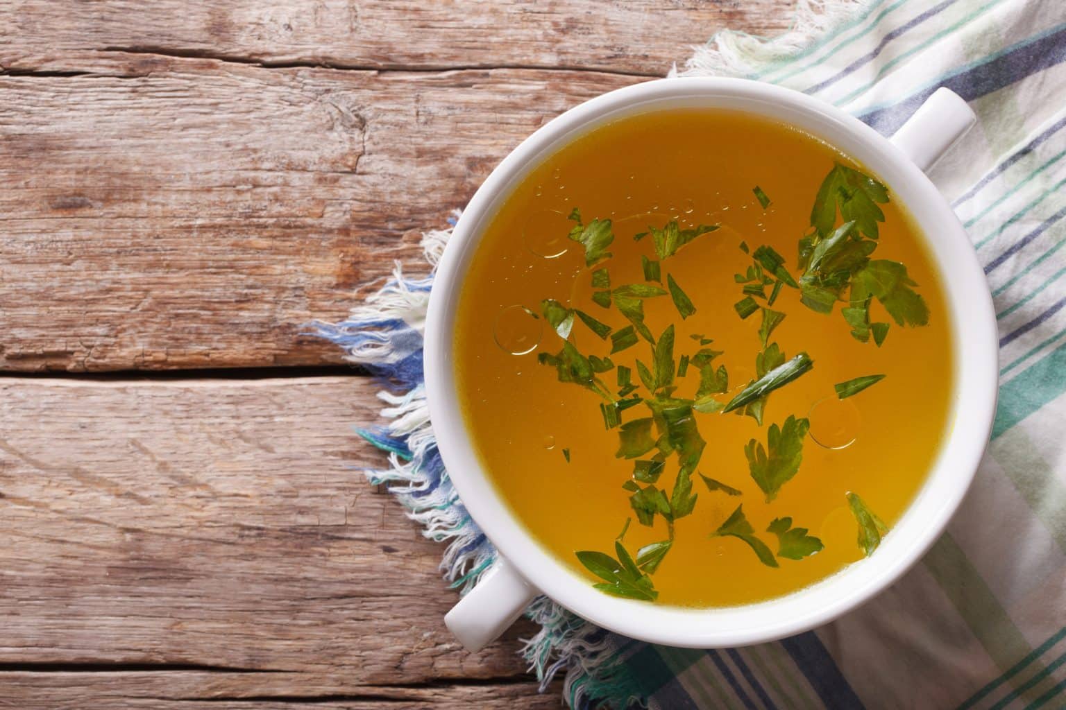 Tasty meat broth with parsley in a white bowl closeup. horizontal view from above