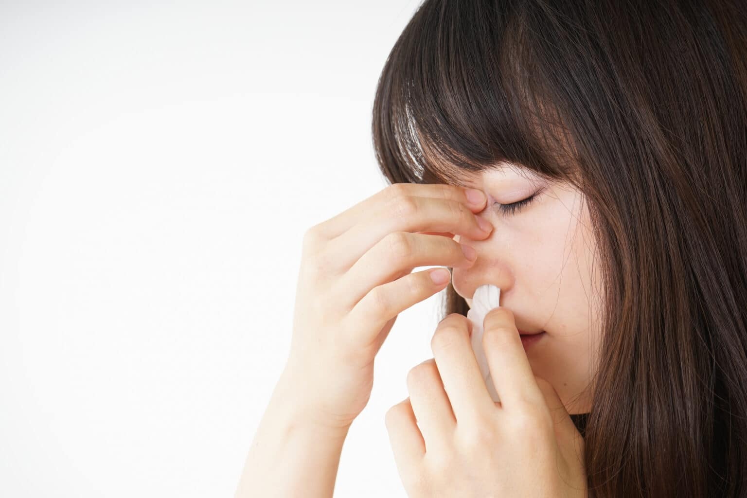 Young woman getting a nosebleed and treating it with a tissue.