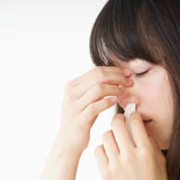 Young woman getting a nosebleed and treating it with a tissue.