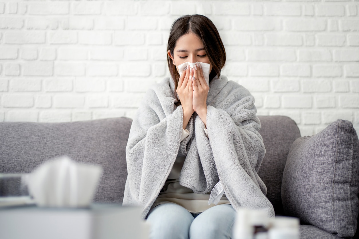 Woman wrapped in a blanket blowing her nose.