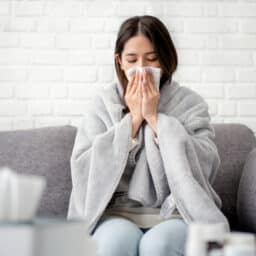 Woman wrapped in a blanket blowing her nose