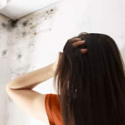 Woman looks at mold on wall in room