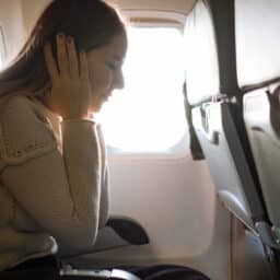 Woman covering her ears in an airplane due to ears popping.